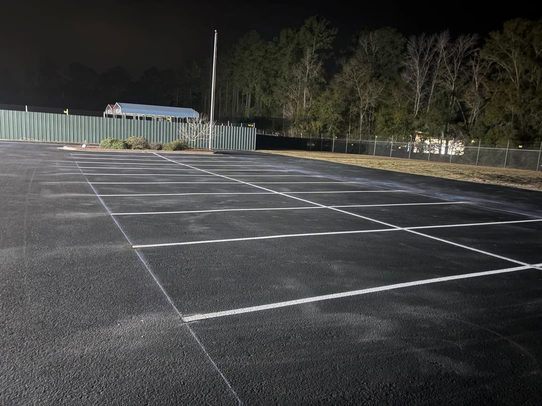 Empty parking lot at night with marked spaces and trees in the background.