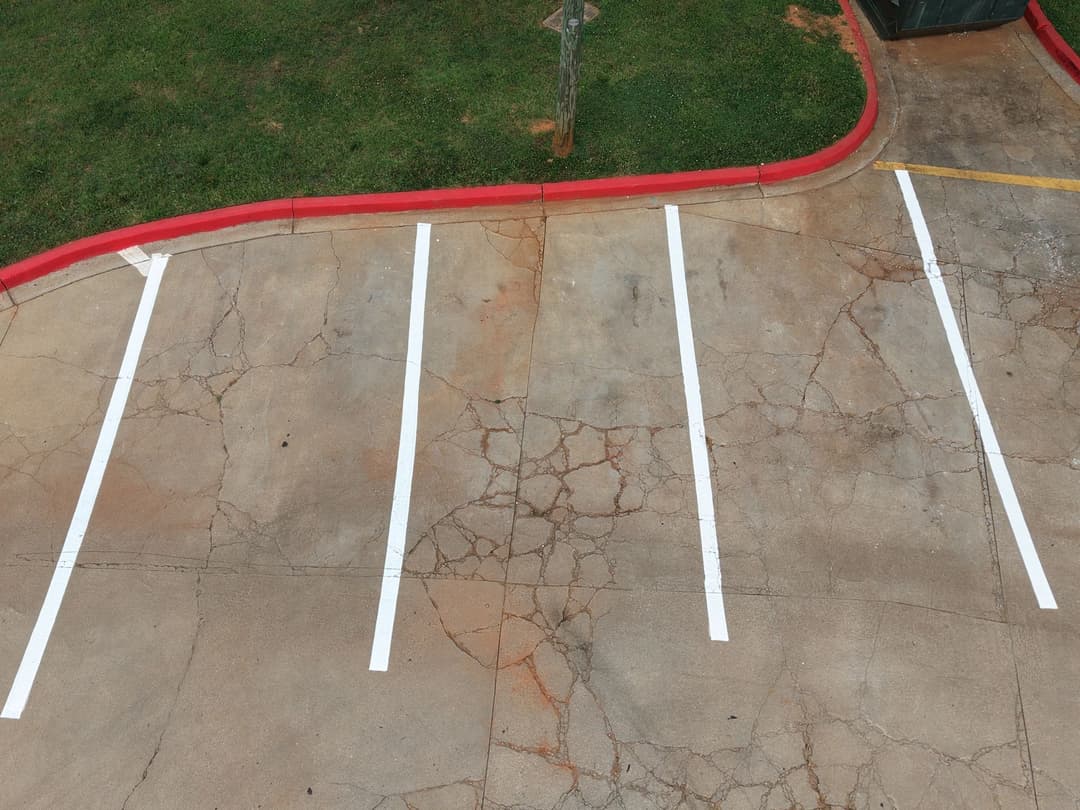 Cracked parking lot surface with white striped lines and red curb.