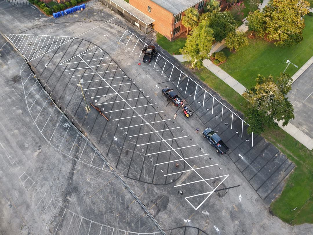 Aerial view of an empty parking lot with unique tire tracks and vehicles partially visible.