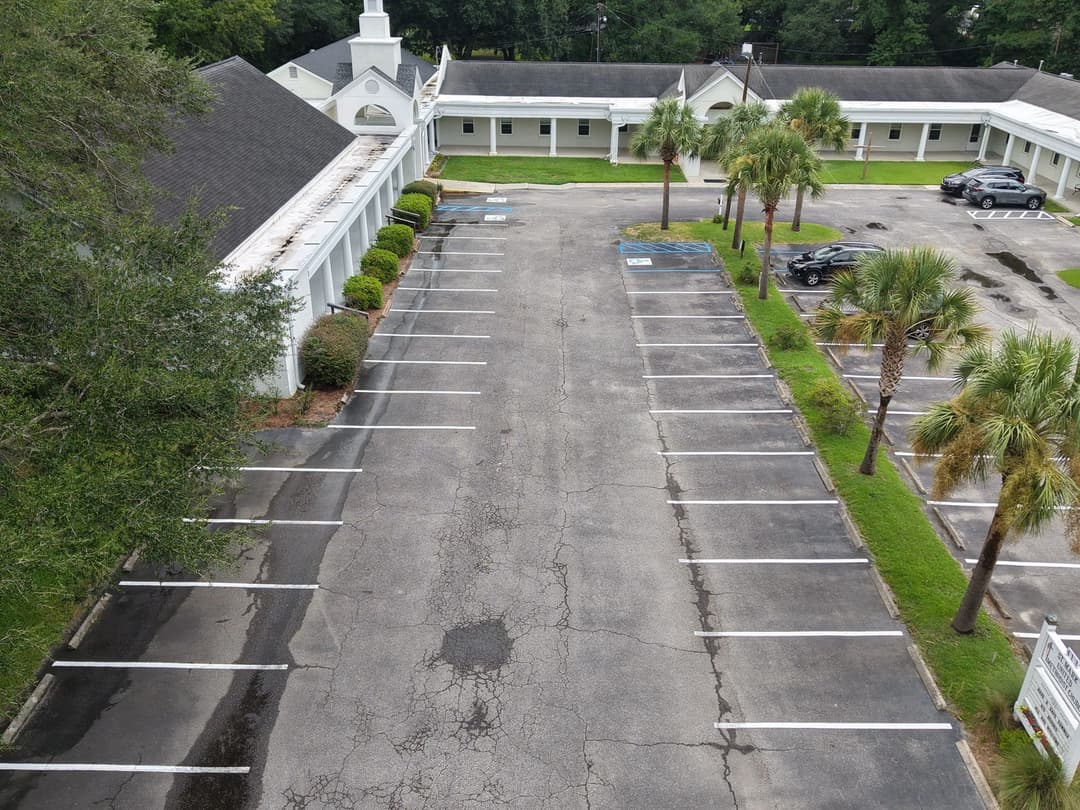 Aerial view of an empty parking lot beside a building and palm trees. Sunny day, clear layout.