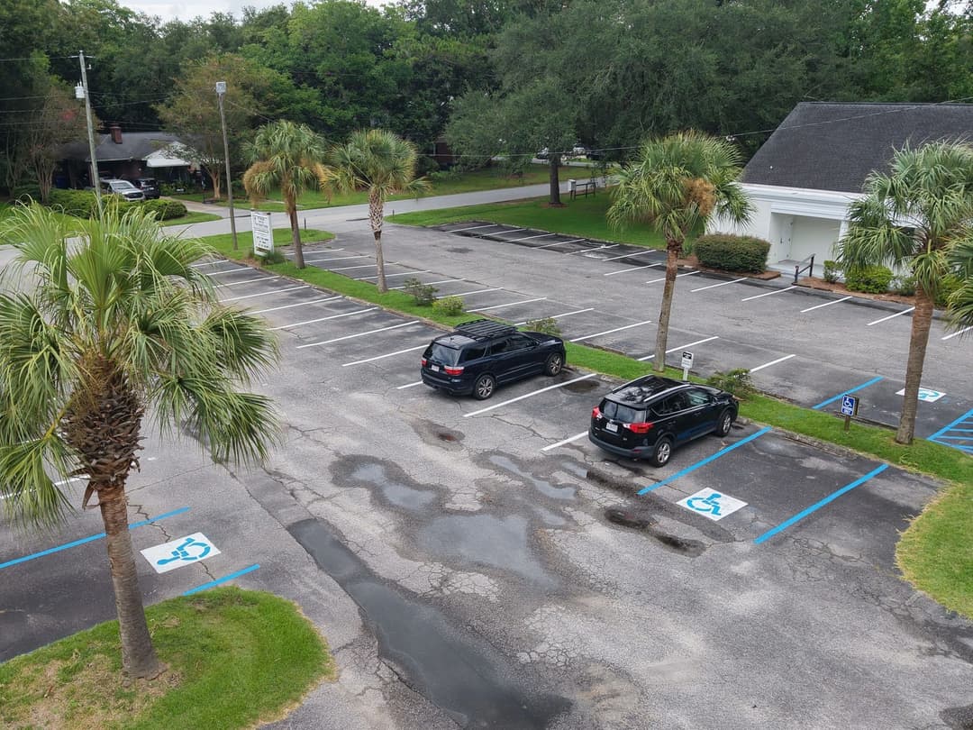 Aerial view of parking lot with two parked cars and accessible parking spaces. Palm trees visible.