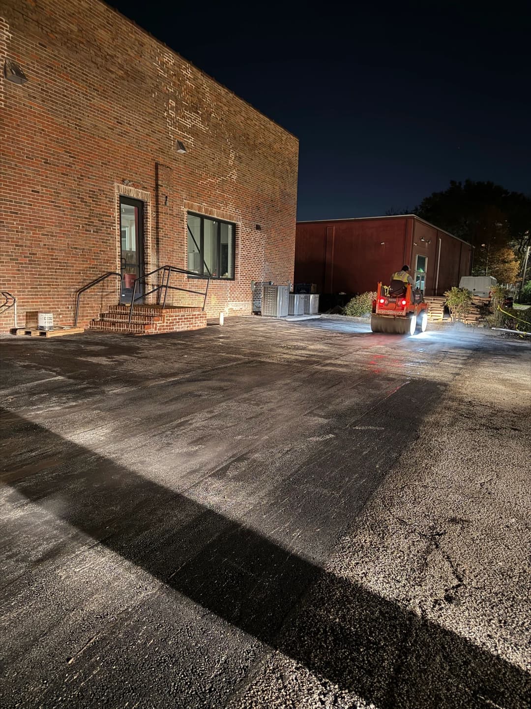 Nighttime view of a parking lot being cleaned with industrial equipment near a brick building.