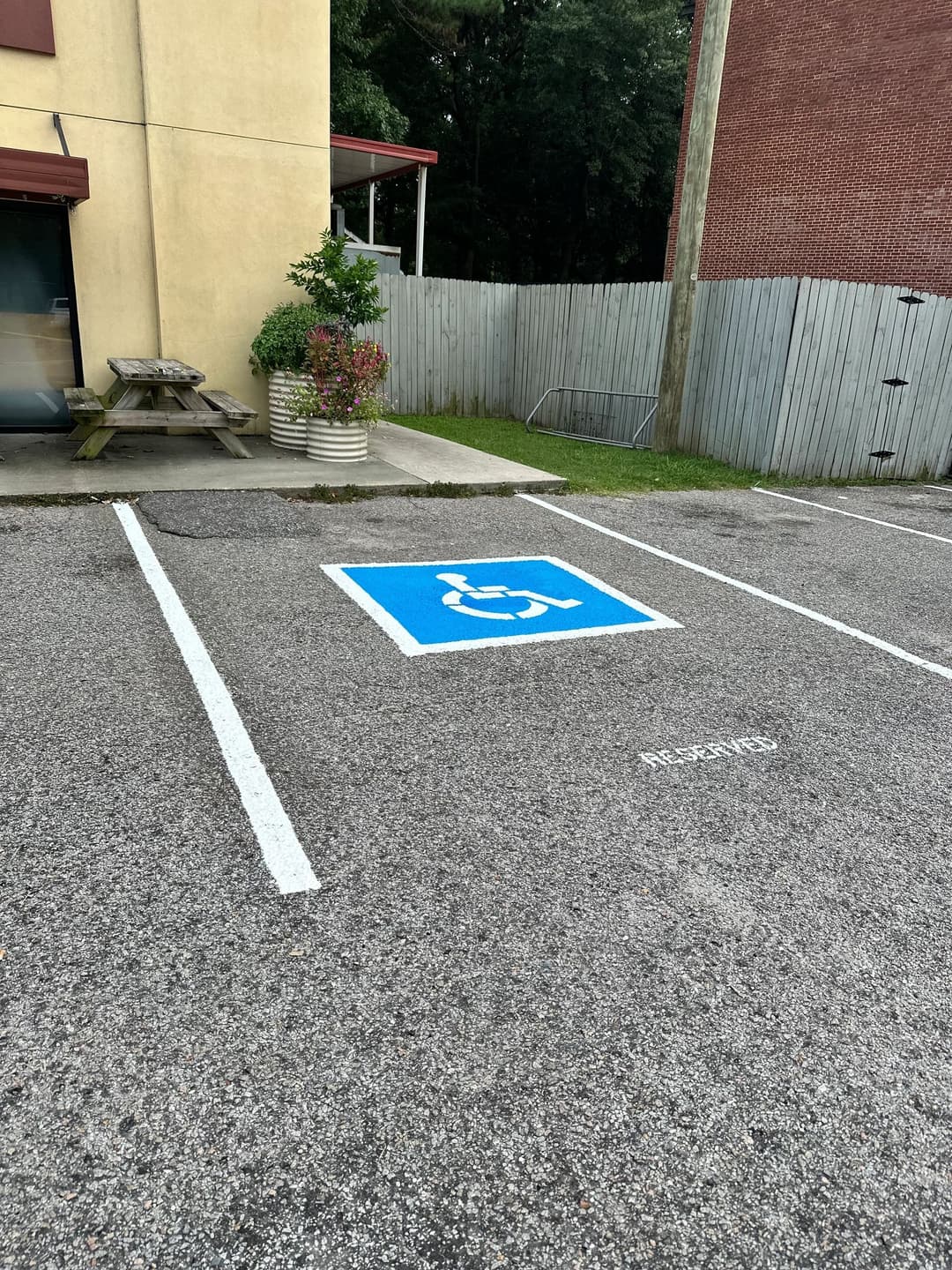 Handicapped parking space with blue symbol, surrounded by greenery and picnic area.